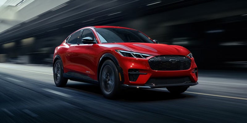 Red Ford Mustang Mach-E electric SUV speeds down a road with motion blur.